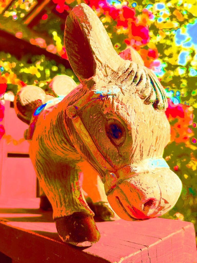 A wooden donkey statue in front of trees.